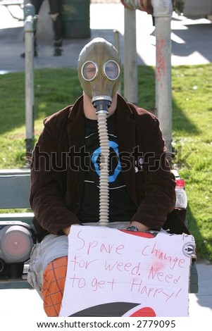 a young man in a gas mask with a sign wants money or weed
