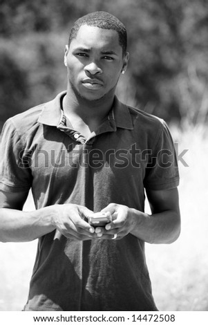 a handsome african american man thinks and responds while he text messages on his cell phone in black and white