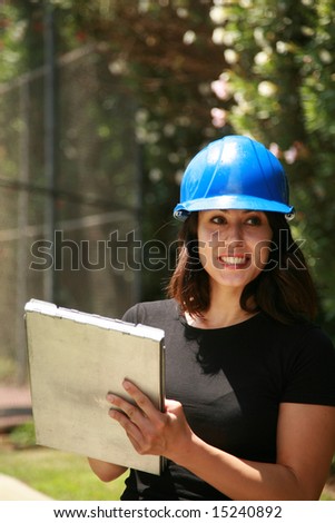 a beautiful young woman in a hard hat is takes notes on a construction site