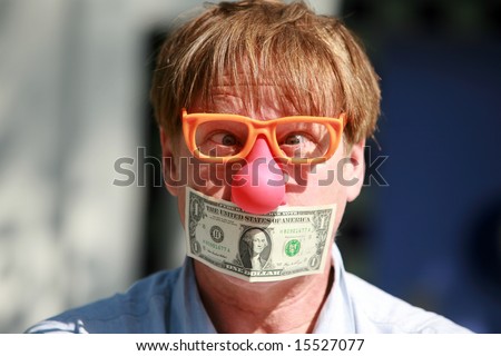 a man wears a rubber clown nose and glasses with a dollar bill taped over his mouth in protest against inflation and the rising cost of goods and services