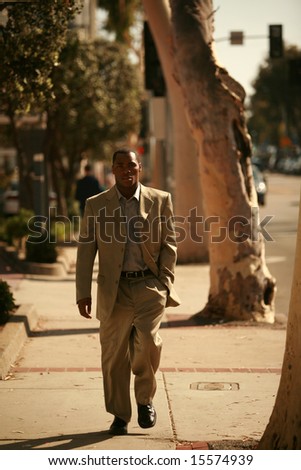 a well dressed american male model walks down a city sidewalk as if he is walking down a cat walk at a fashion show