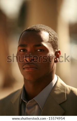 a well dressed african american male model walks down a city sidewalk as if he is walking down a cat walk at a fashion show