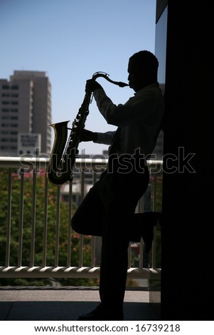 sillouette of a sax player playing his music with a major metropolitan city behind him