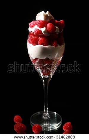Raspberries on black in a cut crystal wine glass with a mirror for reflections with whip cream
