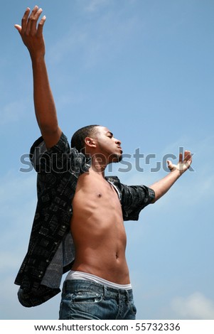 a handsome african american man lifts his arms up into the blue sky in an inspirational image