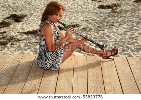 an attractive african american woman plays her clarinet outside at the beach for all to hear and enjoy
