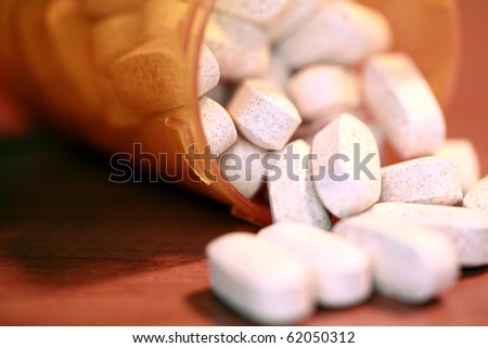 closeup aka macro shot of white pills spilling out of a orange plastic pill bottle on a table. This powerful image can represent, medication, over dose, drug abuse, addiction, medical help, and more