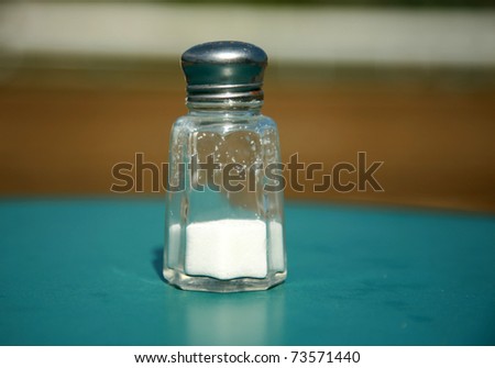 a salt shake half filled with iodized table salt on an table outside with low depth of field