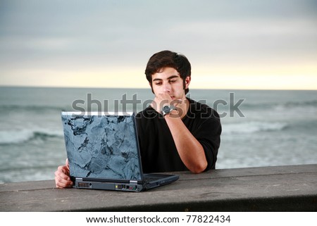 a young man does his school work, or surfs the web on his laptop computer while at the beach. He could be on Spring Break or Summer Vacation or even Skipping School or on the Weekend. You decide
