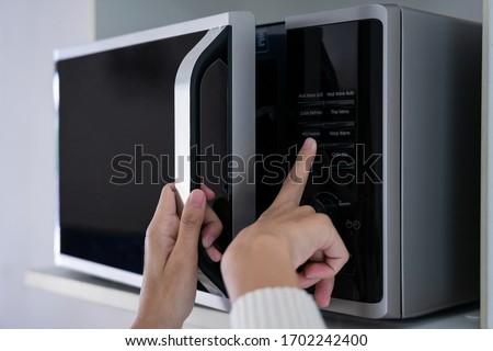 Woman's hands closing the microwave oven door and preparing food in microwave.