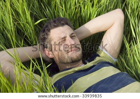 The man lies on a grass having screwed up one eye