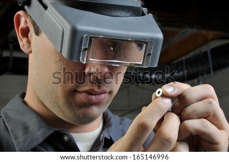 Quality Inspector wearing magnifying glasses inspecting a small manufactured part