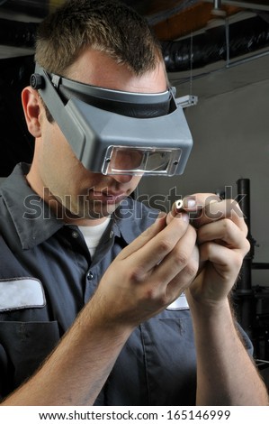 Quality Inspector wearing magnifying glasses inspecting a small manufactured part