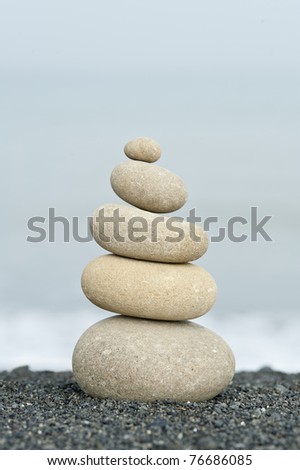 pile of balanced rocks on black sand beach against ocean background