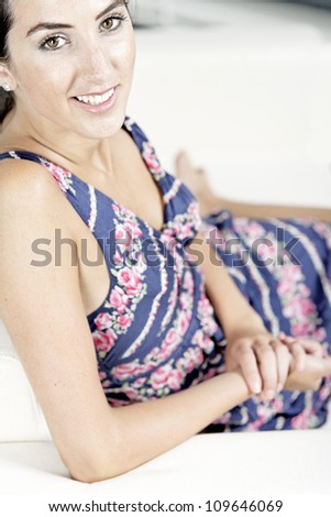 Beautiful young woman wearing a blue summer dress resting on her sofa at home