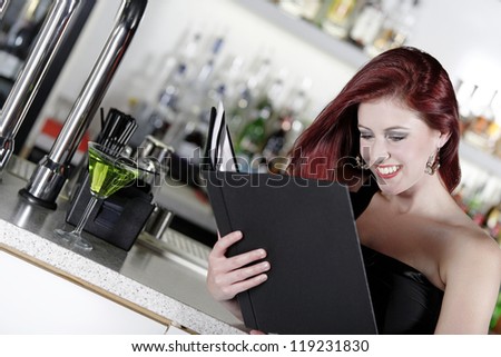 Attractive young woman reading from a wine list at the bar.
