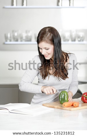 Beautiful young woman reading from a cookery book while cooking in her kitchen.
