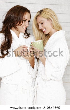 Two young friends in white bath robes chatting and drinking