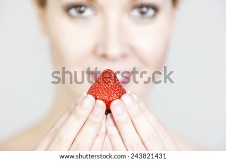 Attractive young woman holding a fresh strawberry to her lips.