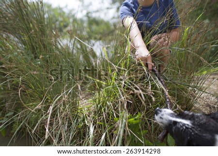 Young boy playing with his dog at the river with a stick