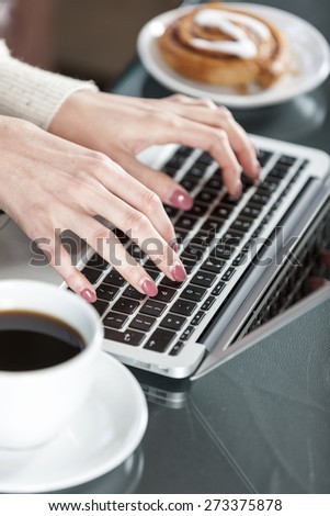 Woman\'s hands typing on a laptop keyboard with coffee and fresh cake