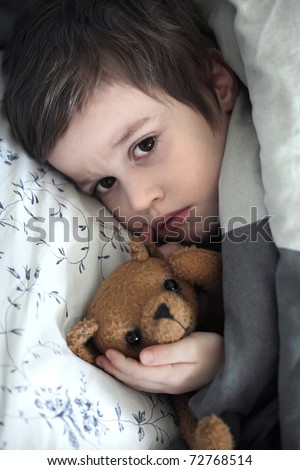 Small boy with teddy bear toy in the bed
