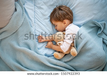 Photo of baby boy sleeping together with teddy bear. His favorite napping spot. Adorable kid boy after sleeping in bed with toy. Boy sleeping on bed with teddy bear. Sleepyhead