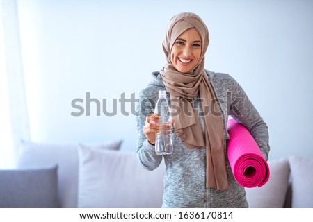 Fit young muslim woman drinking water . Young muslim woman ready to running. Young muslim woman holding bottle of water and fitnes mate. Portrait of muslim woman likes her active life.