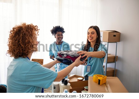 Volunteers Collecting Food Donations In Warehouse. Team of volunteers holding donations boxes in a large warehouse. Volunteers putting clothes in donation boxes, social worker making notes charity