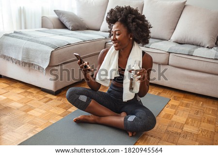 Woman using smart phone on exercise mat in front of her laptop. Sporty girl is exercising at phone on mat enjoying playlist on mobile phone. Positive active energtic sportswoman sit on mat use phone Сток-фото © 