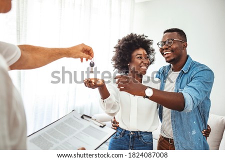 Handsome realtor is giving key to the new apartment to happy young couple. Couple buying new apartment.  A young couple receive the keys to their new apartment from a letting agent.