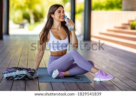 Photo of young Woman drinking water from bottle. Caucasian female drinking water after exercises or sport. Beautiful fitness athlete woman drinking water after work out exercising on sunset evening