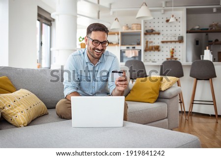 Handsome man with laptop and credit card at home, portrait. Shot of a handsome young businessman using a computer while holding a credit card in an home office