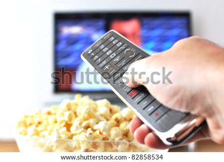 stock-photo-remote-control-in-the-hand-against-pop-corn-and-tv-set-82858534.jpg