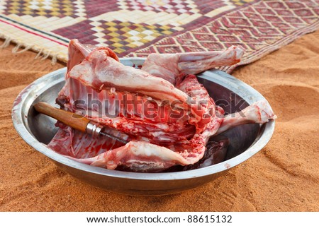 Freshly slaughtered goat meat in a bowl in the desert sand.