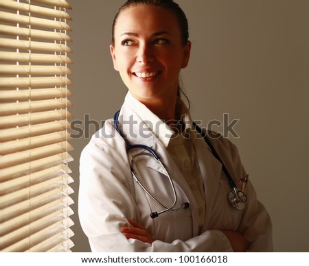 Woman doctor is standing near window with folded arms