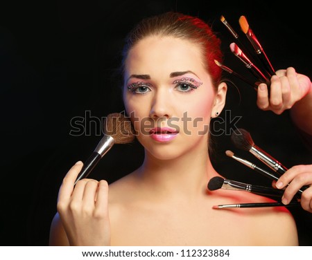 Beautiful young adult woman holds the make-up brushes near attractive face.