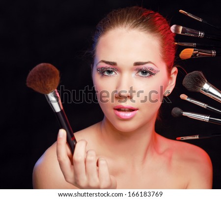 Beautiful young adult woman holds the make-up brushes near attractive face