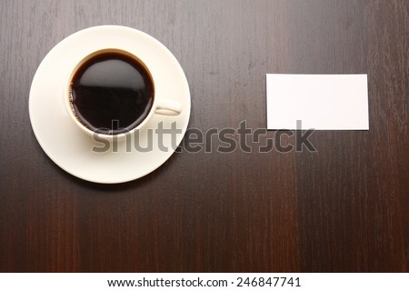 A cup of coffee and a note card from a wooden desk from above