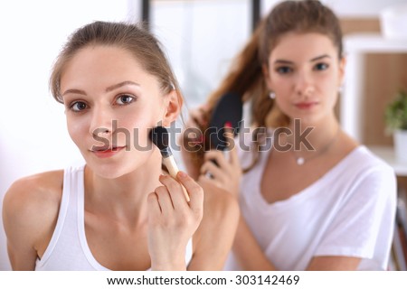 Beautiful girls looking in the mirror and applying cosmetic with a big brush