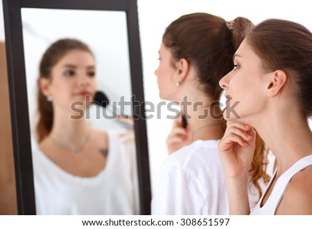 Beautiful girls looking in the mirror and applying cosmetic with a big brush