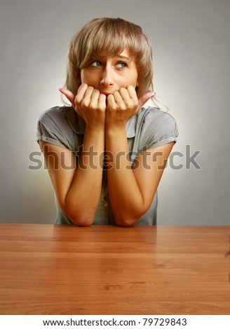 A young frightened woman sitting at the desk, isolated on grey