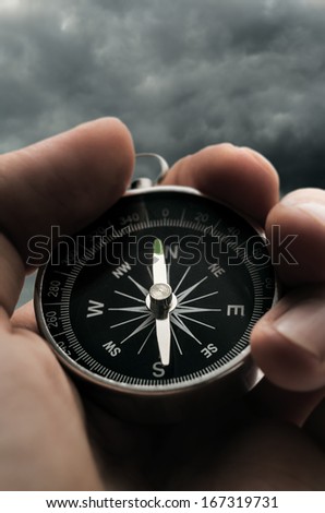 Hand holding black compass on stormy sky background