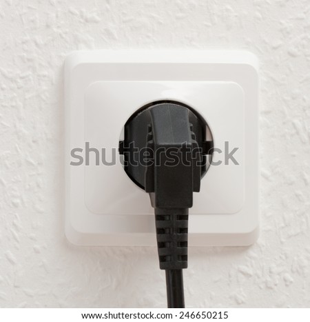 Single electric socket with plug on white wall