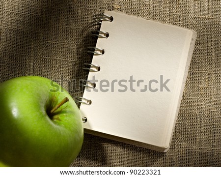 Notepad and apple on the sacking background
