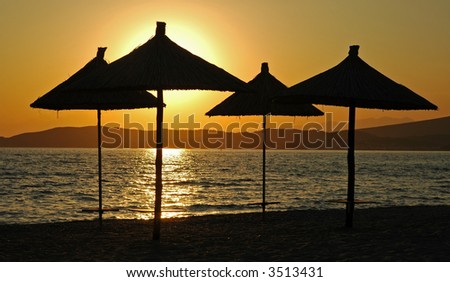 Dramatic sunset on the paradise beach, sun glow reflecting on the sea surface, making silhouettes from parasols