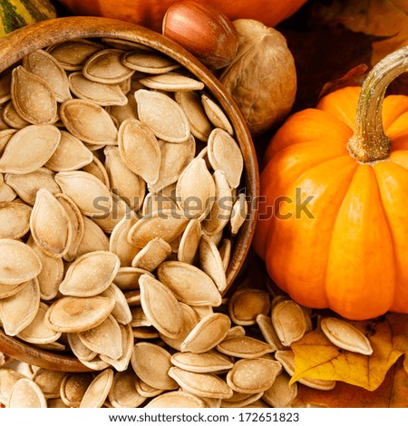 Toasted, salted pumpkin seeds spilling from a wooden bowl, accented with nuts and a small pumpkin