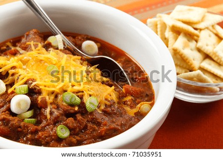 A hearty bowl of chili topped with shredded cheese and scallions makes a tasty lunch or dinner