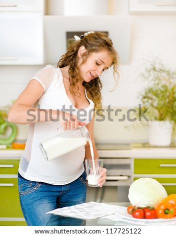 Beautiful pregnant mother pour out milk into glass on the house kitchen