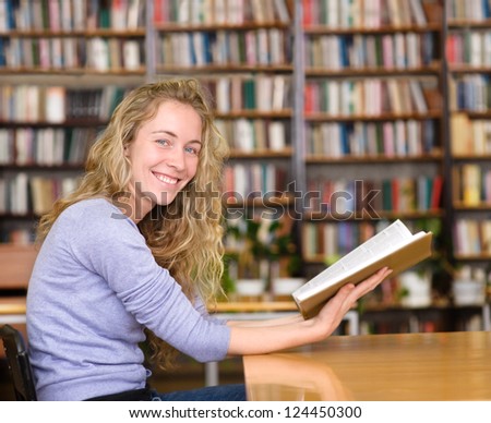 female student reads the book in library. looking at camera